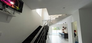 Un intérieur moderne avec un escalier, un coin repas et un téléviseur fixé au mur.