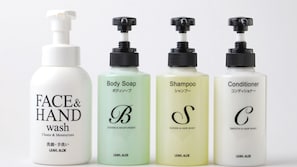 Four bottles of skincare products labeled FACE&HAND wash, Body Soap, Shampoo, and Conditioner, each with a pump dispenser and labeled with a letter and product type.