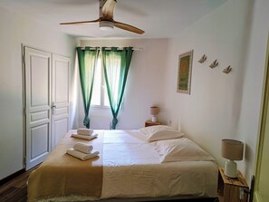 A bedroom with a bed, a ceiling fan, a nightstand with a lamp, and a window with curtains.