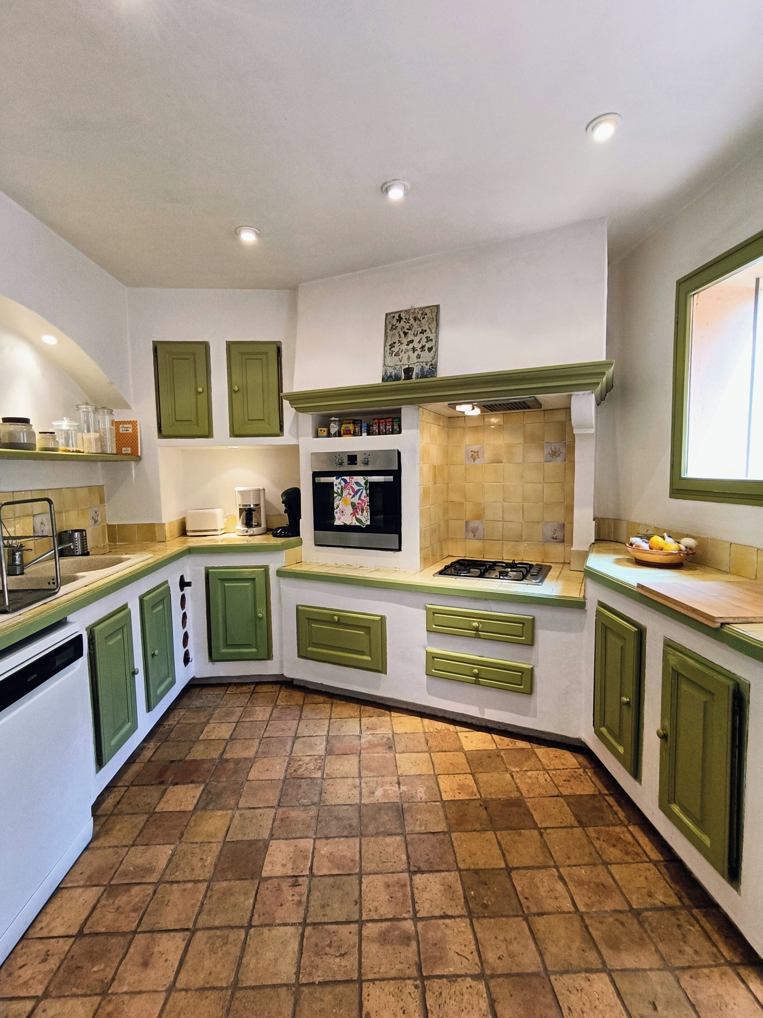 Une cuisine avec des meubles de couleur verte, un pare-feu en carreaux et un sol carrelé.