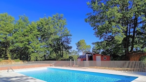 A rectangular swimming pool with a tiled deck, surrounded by a white fence, trees, and a small building with a red roof. - Au coeur des ocres - Charming vacation home (Roussillon)