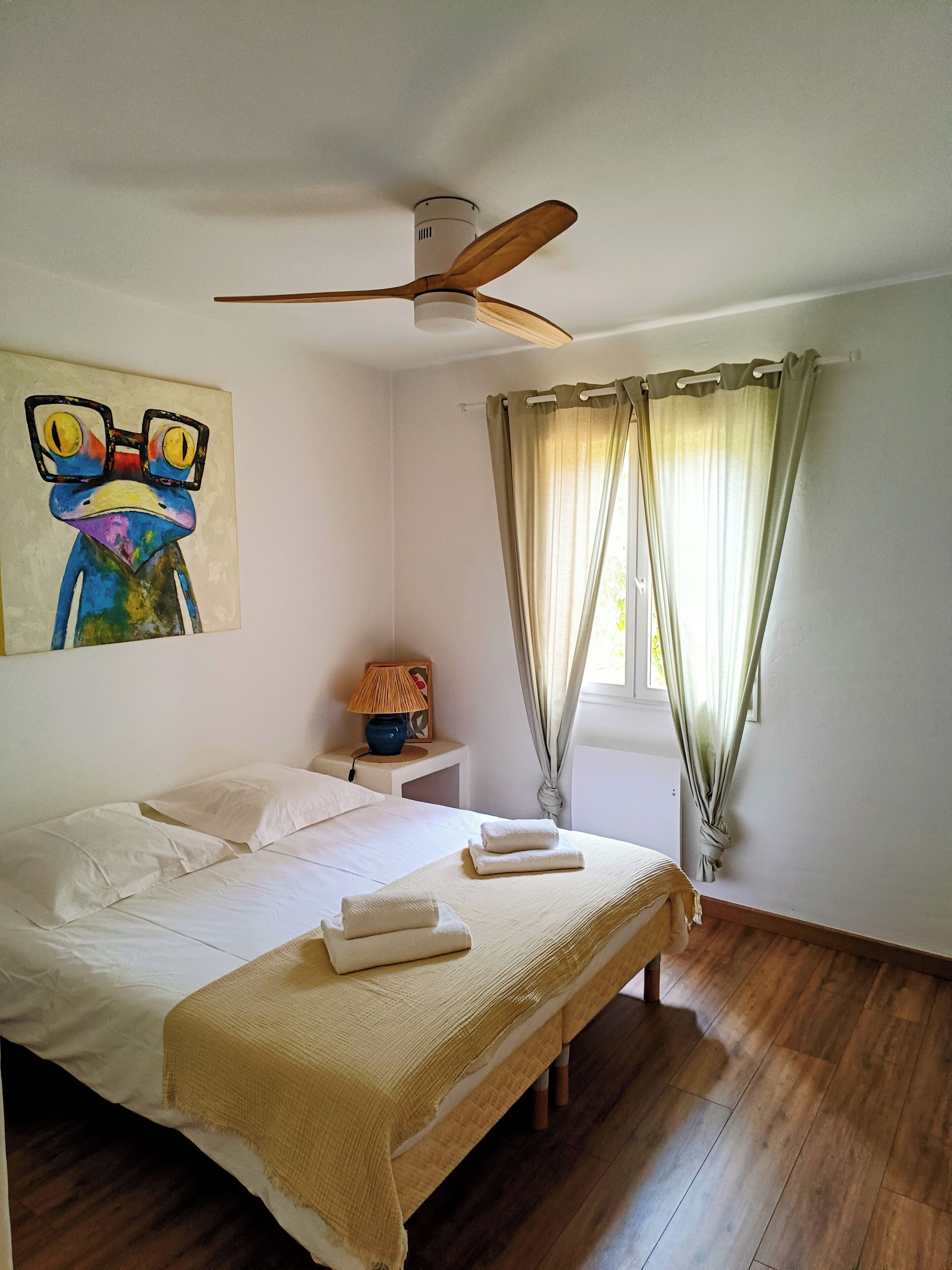 Une chambre à coucher avec un lit, un ventilateur de plafond, une table de chevet, une lampe et un tableau au mur.
