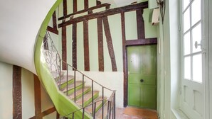 A spiral staircase with a green handrail and wooden balusters, leading to a green door with a window above it.