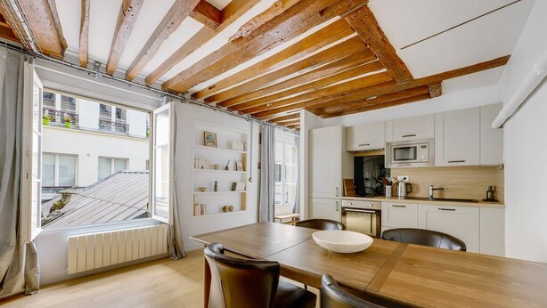 A modern kitchen with white cabinets, a microwave, and a stove. There is a dining area with a wooden table and chairs.