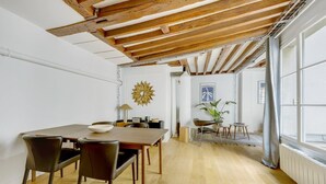 A dining area with a wooden table and chairs, a decorative wall piece, and a view through an open door to a room with a plant.