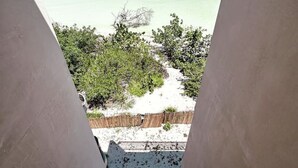 A view from a balcony overlooking a beach with clear turquoise water and a sandy shore. - Golden Hour 2BR Ocean View Apt (Holbox)