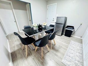 Eine kleine Küche mit Esstisch, Stühlen, einem Kühlschrank und einem Mülleimer.