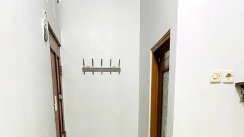 Un pasillo estrecho con piso de baldosas, una puerta de madera, un pequeño bote de basura y un tapete blanco y rojo a cuadros.
