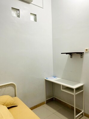 A small, clean room with a bed, a desk, and a shelf. - IB Homestay Syariah by EcommerceLoka (Tegal)
