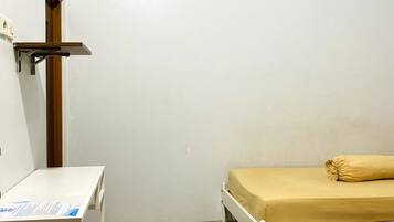 A small, clean room with a bed, a desk, and a trash bin.