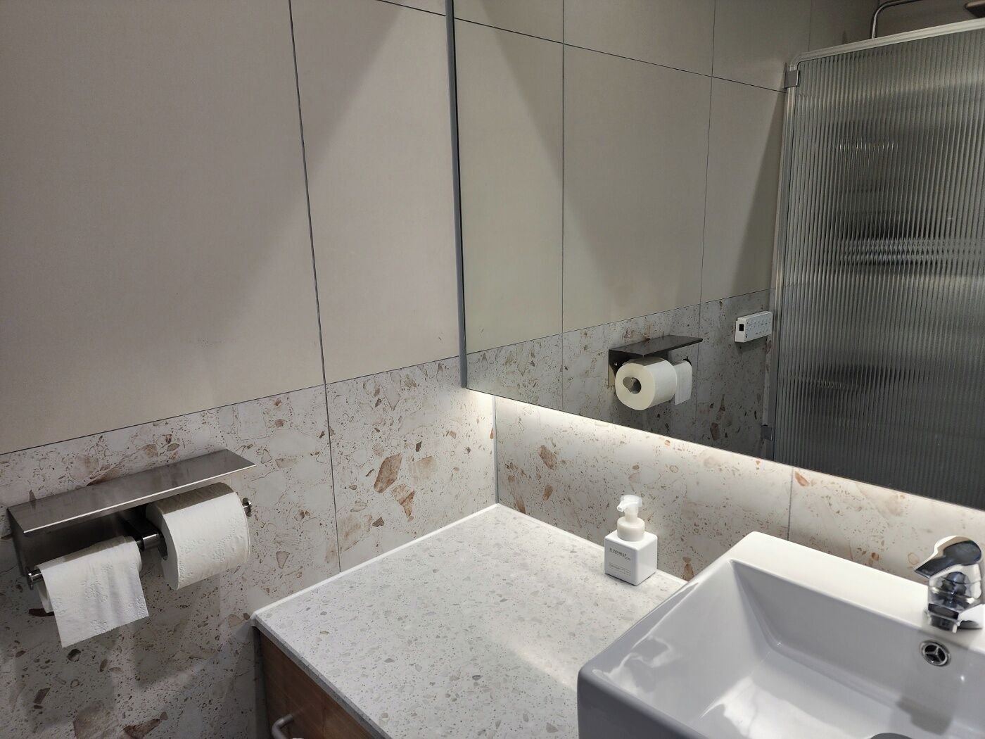 Un baño con encimera de mármol, un lavamanos, un dispensador de jabón y un espejo.