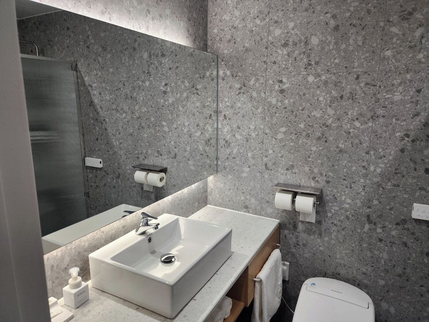 A modern bathroom with a rectangular sink, a mirror, and two toilet paper holders on the wall.
