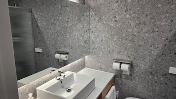 A modern bathroom with a rectangular sink, a mirror, and two toilet paper holders on the wall.