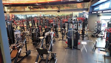 A gym with various exercise machines, a mirrored wall, and a ceiling with a unique design.