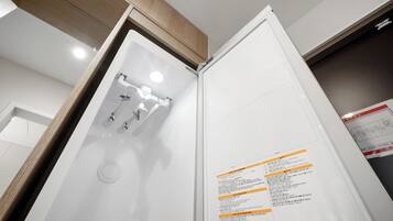 A bathroom with a white shower enclosure, a mirror, and a wall-mounted control panel with instructions.
