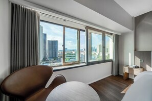 A modern hotel room with a large window offering a city view, a comfortable chair, a small desk, and a bedside table. - Crystal Hotel (Daegu)