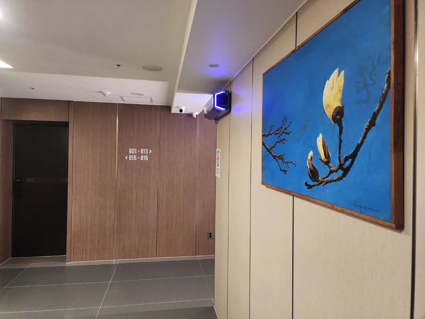 A hallway with wooden paneling, a blue painting of a bird on a branch, and a sign with room numbers.