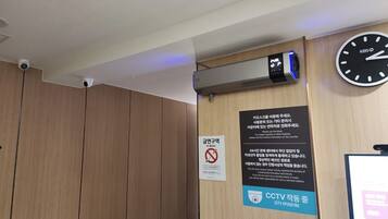 A room with a wooden panel wall, a clock, a CCTV camera, and a no-smoking sign.