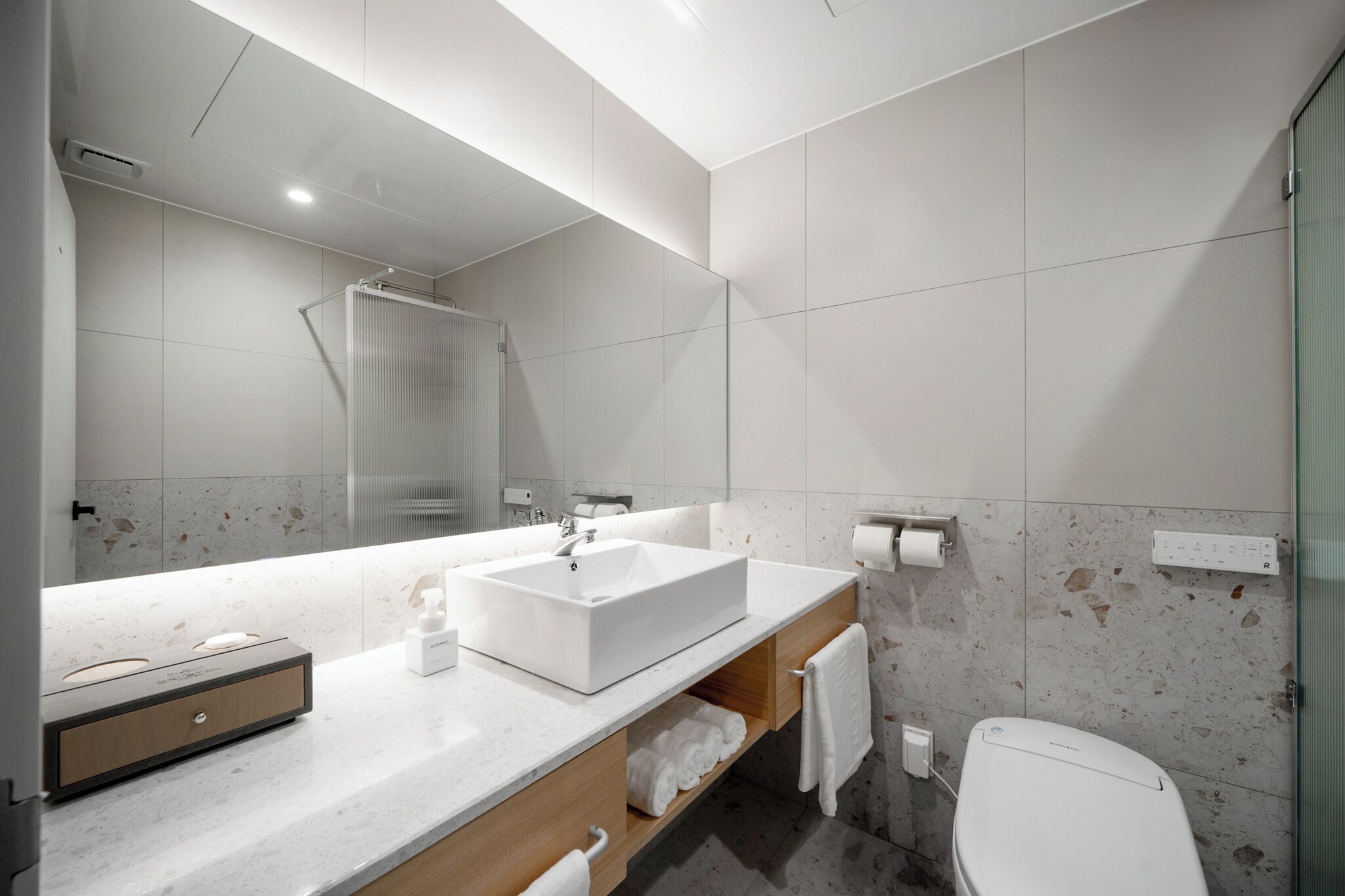 A modern bathroom with a large mirror, a white sink, a shower, and a toilet.