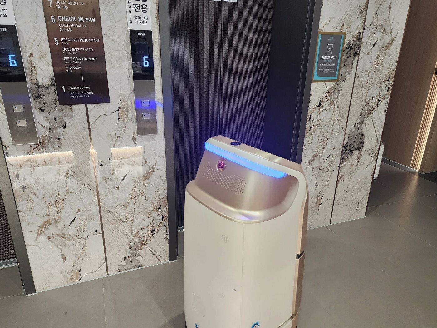 Ein Aufzug mit digitaler Anzeige für die 6. Etage, einem Schild für Gästezimmer und einem Check-in-Schild.