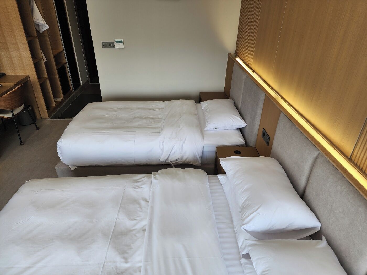 A hotel room with two single beds, a wooden headboard, a small desk, and a chair.
