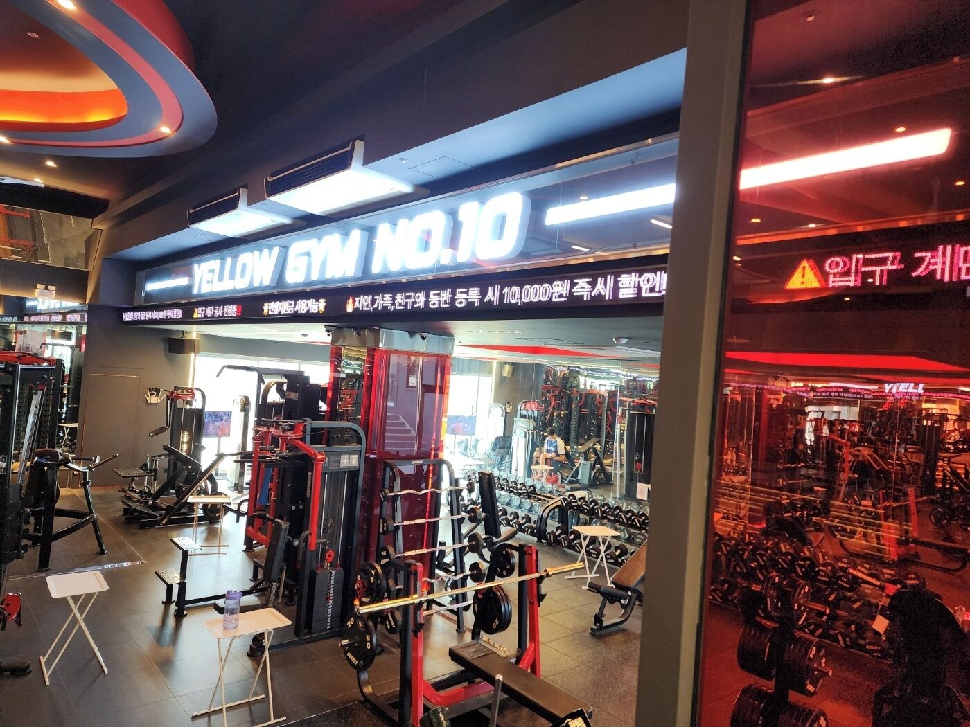 A gym interior with various exercise equipment, a weightlifting area, and a mirrored wall.