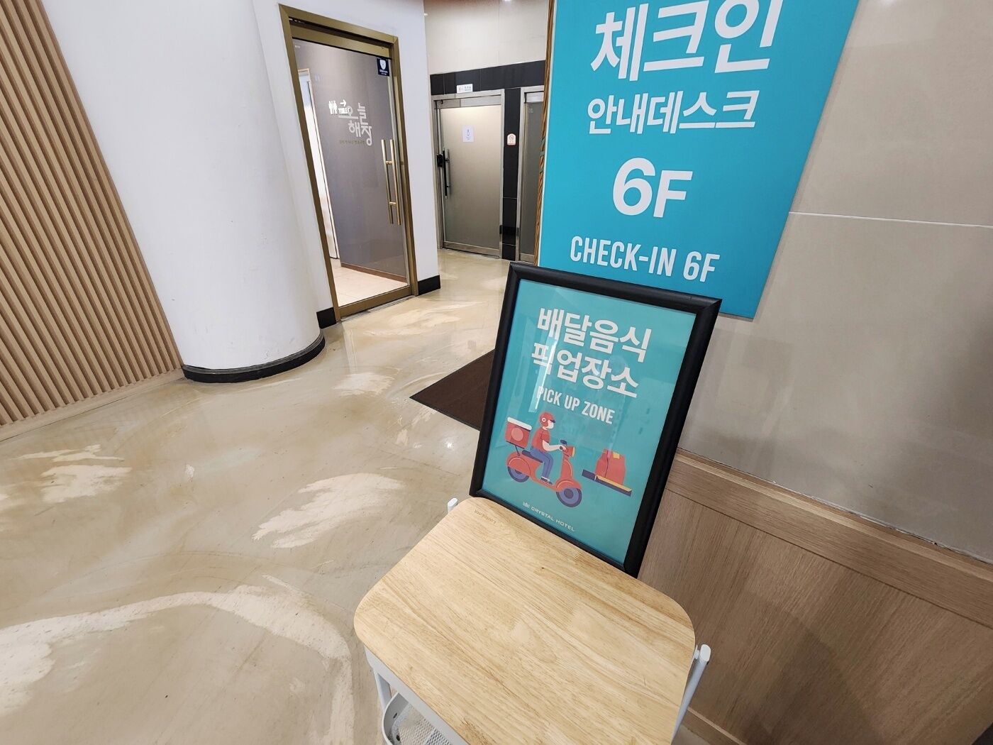 A hotel lobby with a check-in desk, a sign indicating a pick-up zone, and a door in the background.