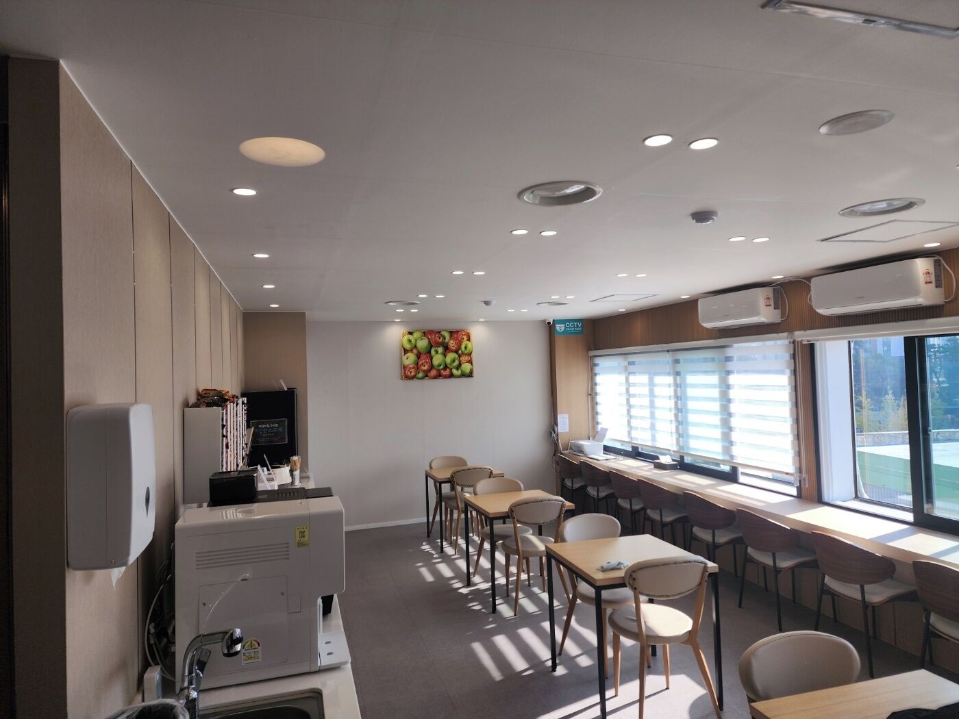 A modern conference room with a long table and chairs, a large window with blinds, and a wall-mounted CCTV camera.