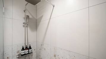 Eine Dusche mit Duschbrause, Wandarmatur und drei Shampoo-Flaschen auf einem Regal.