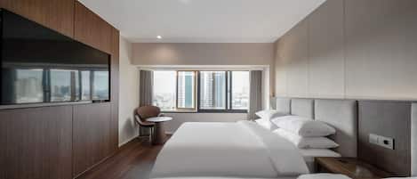 A modern hotel room with a large bed, a seating area, and a view of the city.