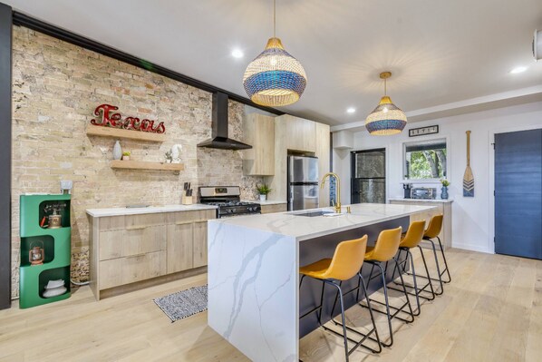 A modern kitchen with a large island, wooden cabinets, and a brick accent wall.
