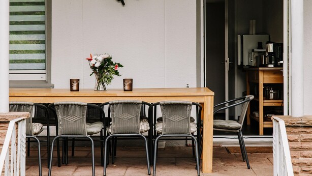 A dining area with a wooden table, wicker chairs, a vase with flowers, and a black butterfly decoration on the wall.
