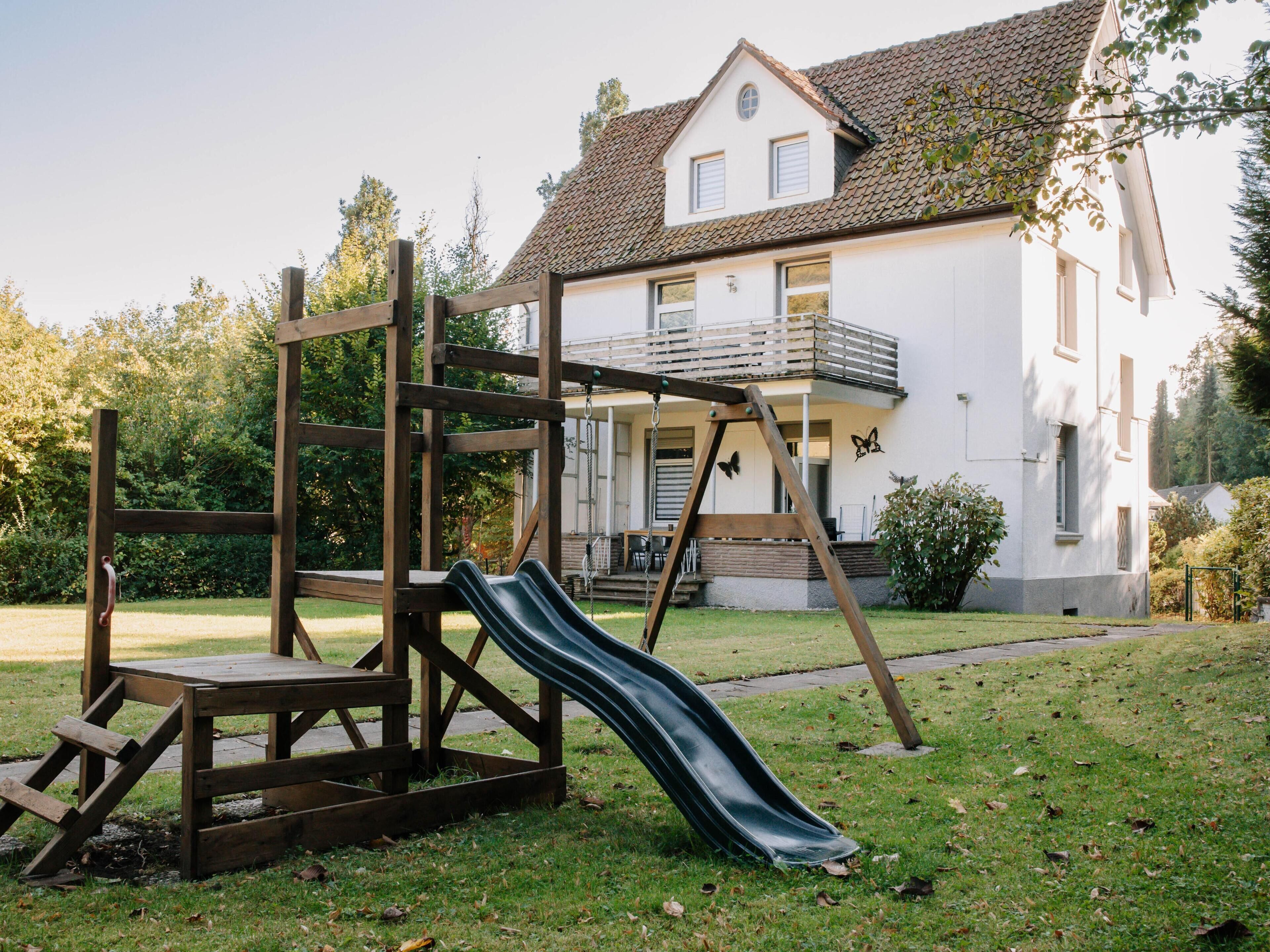 Ein Spielplatz mit Rutsche und Klettergerüst vor einem weißen Haus mit Balkon.