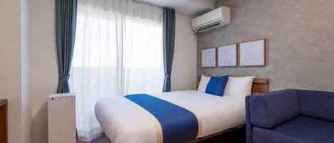 A hotel room with a bed, a blue armchair, an air conditioning unit, and a window with curtains.