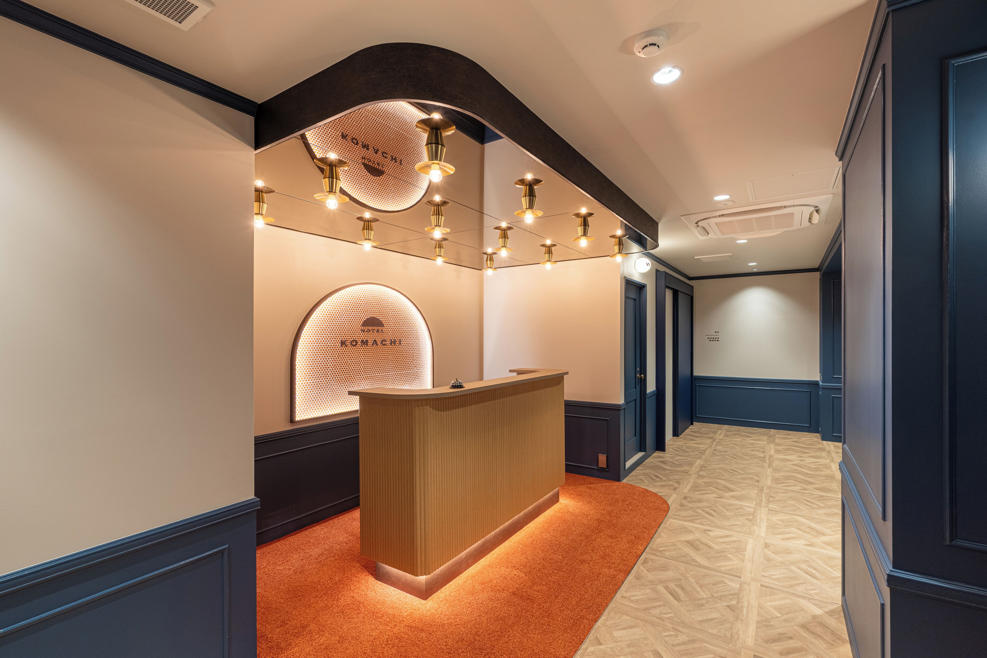 Un espace d’accueil avec un comptoir de réception en bois, un mur décoré d’un motif et une moquette à motifs.