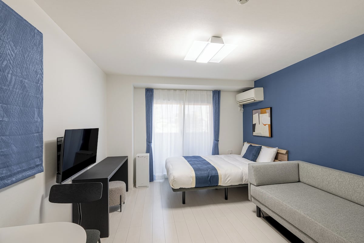 Une chambre moderne avec un lit, un canapé, un bureau avec une télévision et une fenêtre avec des rideaux.