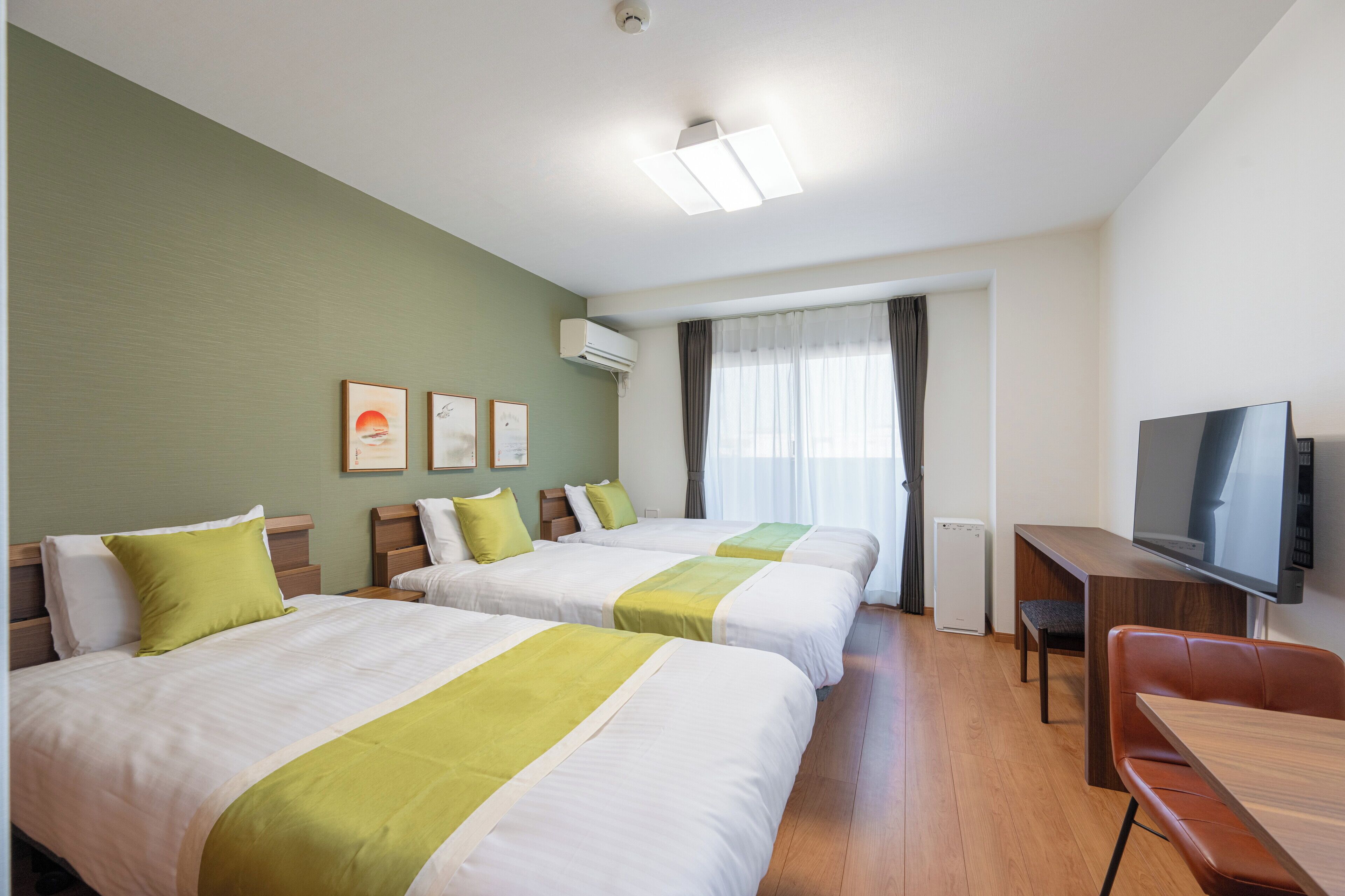 Quarto de hotel com duas camas, televisão, escrivaninha e janela com cortinas.