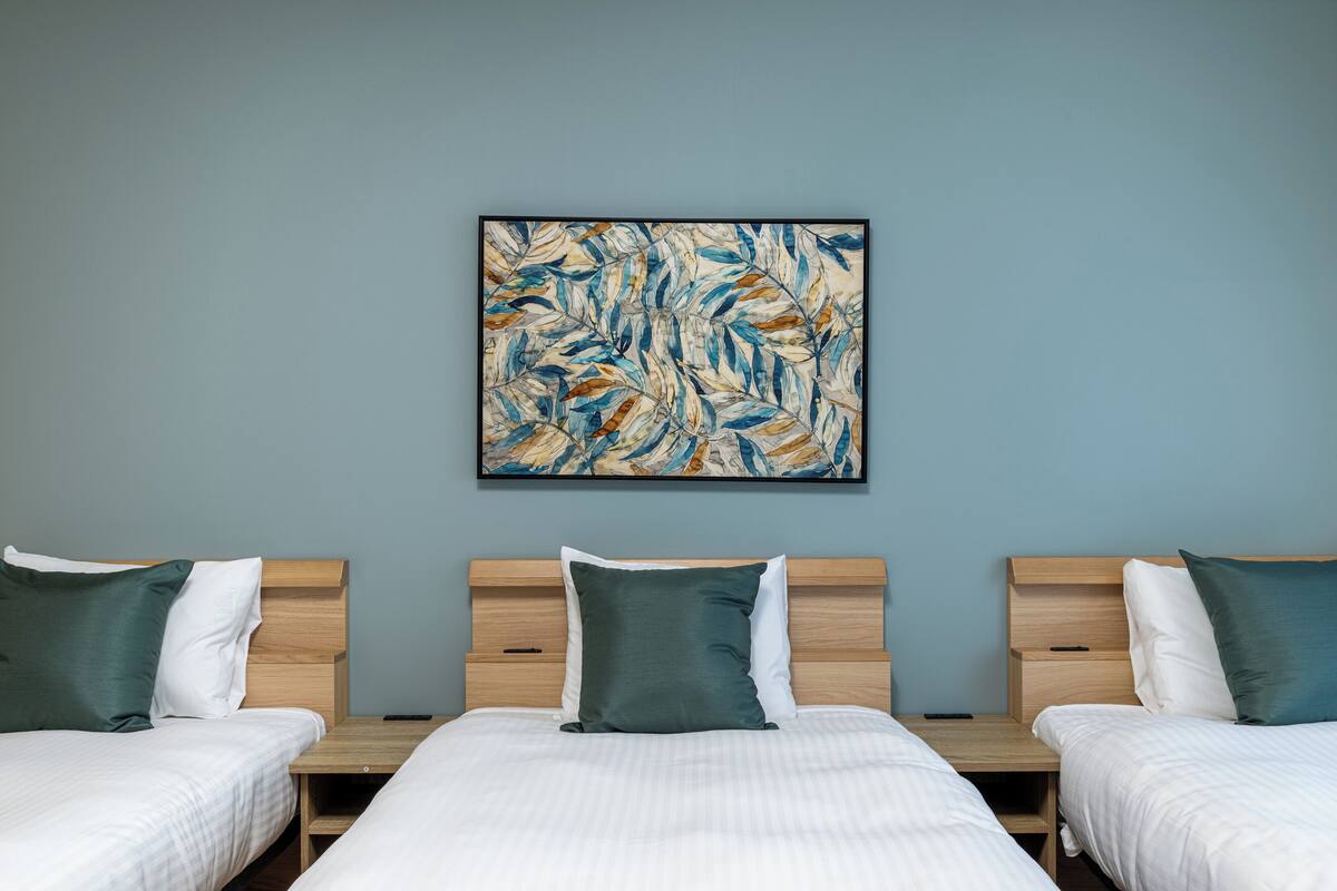 Une chambre d’hôtel avec deux lits, chacun doté d’une tête de lit en bois, de draps blancs et d’oreillers verts. Un grand tableau abstrait est accroché au mur, au-dessus des lits.