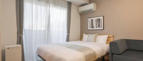 Un dormitorio con una cama, un sofá gris, un aire acondicionado blanco y una obra de arte enmarcada en la pared.