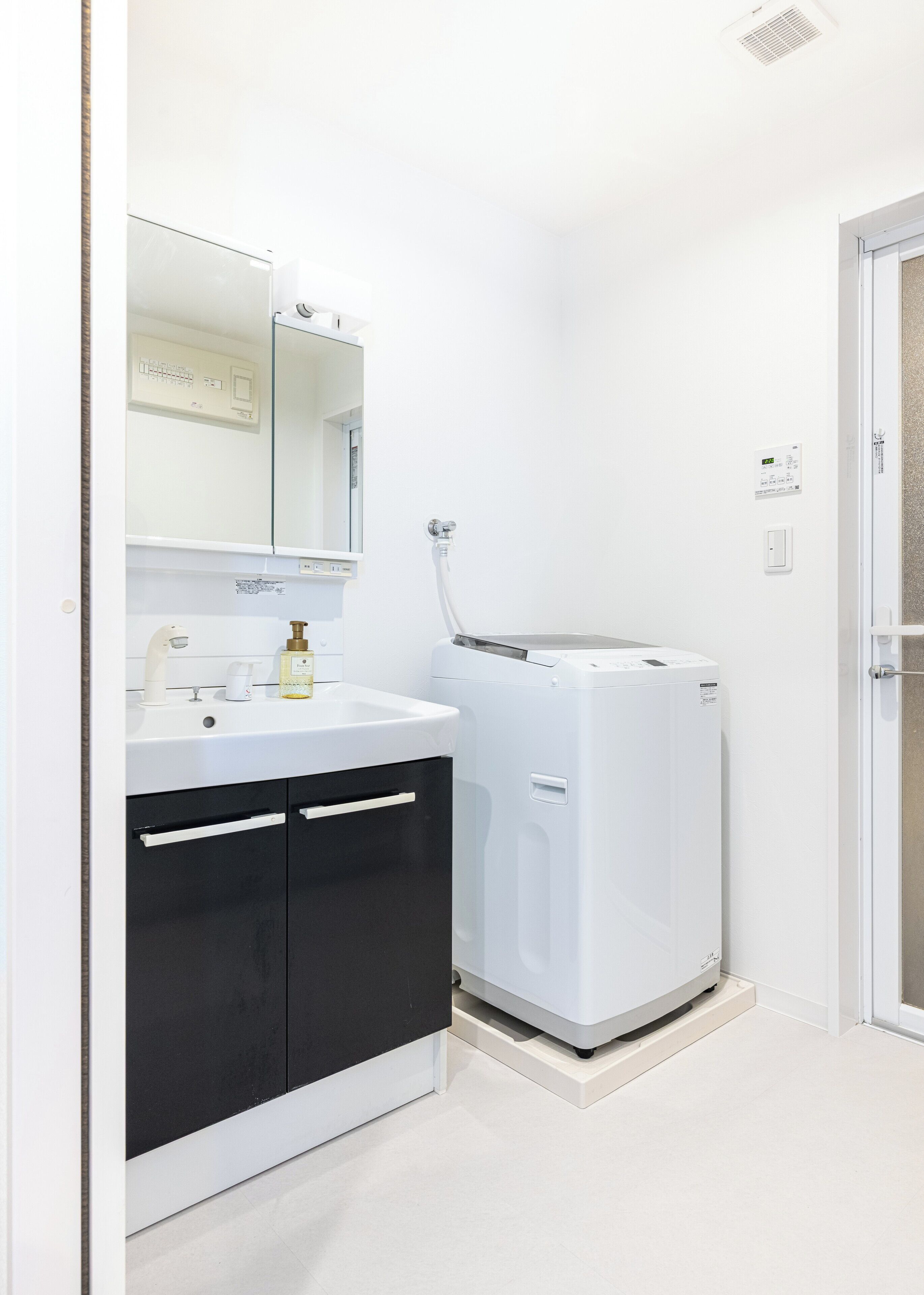 Ein kleines Badezimmer mit einem weißen Waschbecken, schwarzen Schränken, einem Spiegel und einer weißen Waschmaschine.