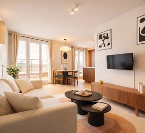 Quarto de hotel moderno com sofá, mesa de jantar, televisão e uma janela grande.