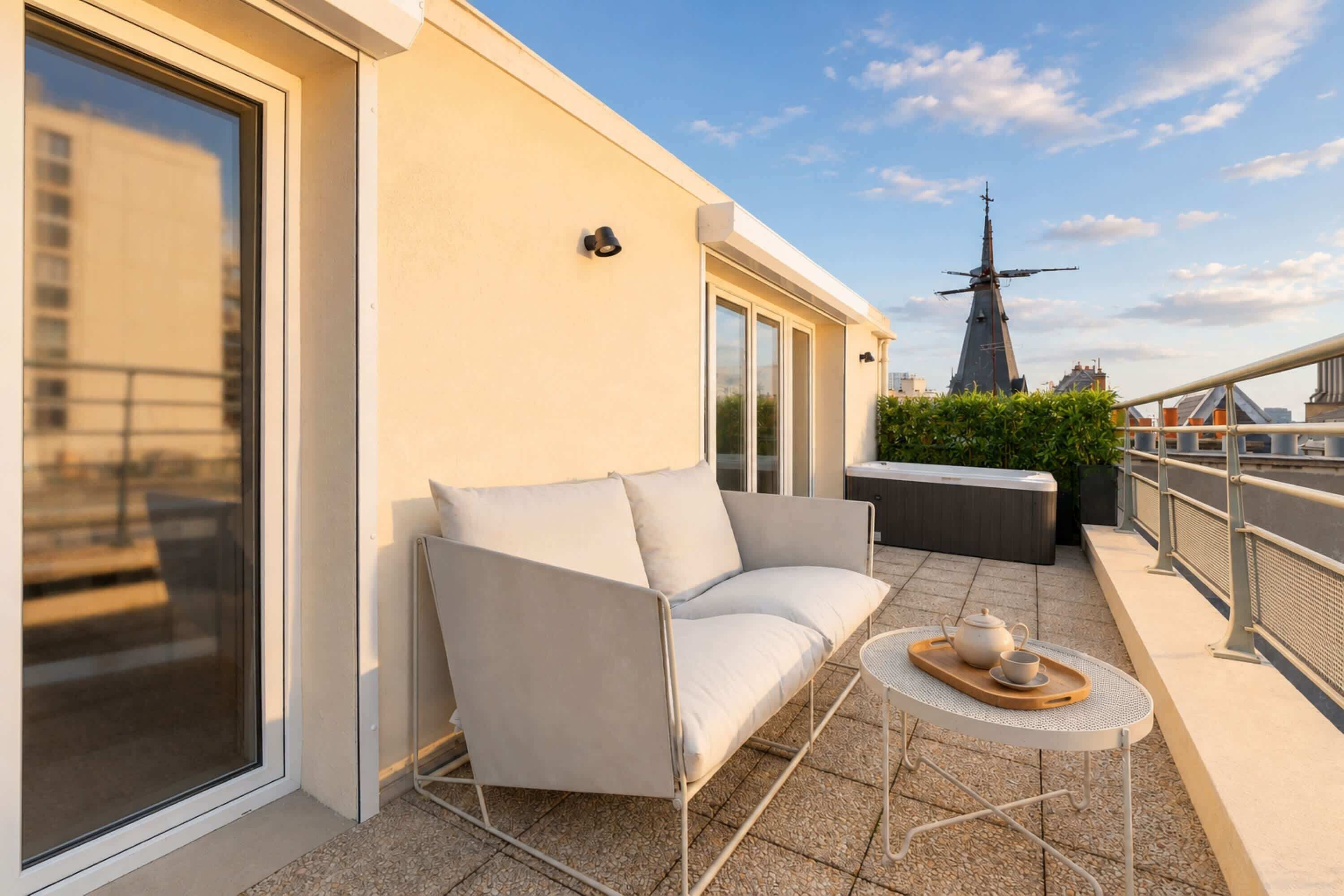 A balcony with a white sofa, a small round table with a teapot and cup, and a windmill in the background.