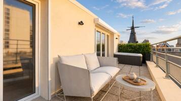 Un balcon avec un canapé blanc, une petite table ronde sur laquelle se trouvent une théière et une tasse, et un moulin à vent en arrière-plan.