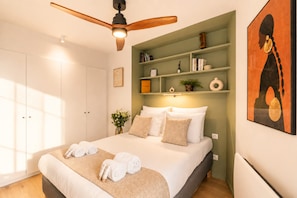 Un dormitorio con una cama, ventilador de techo, estantería y un cuadro.