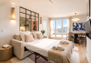 A modern hotel room with a bed, a desk, a chair, a TV, and a large window with a city view. - Loft with terrace, jacuzzi & lift near Invalides (Paris)