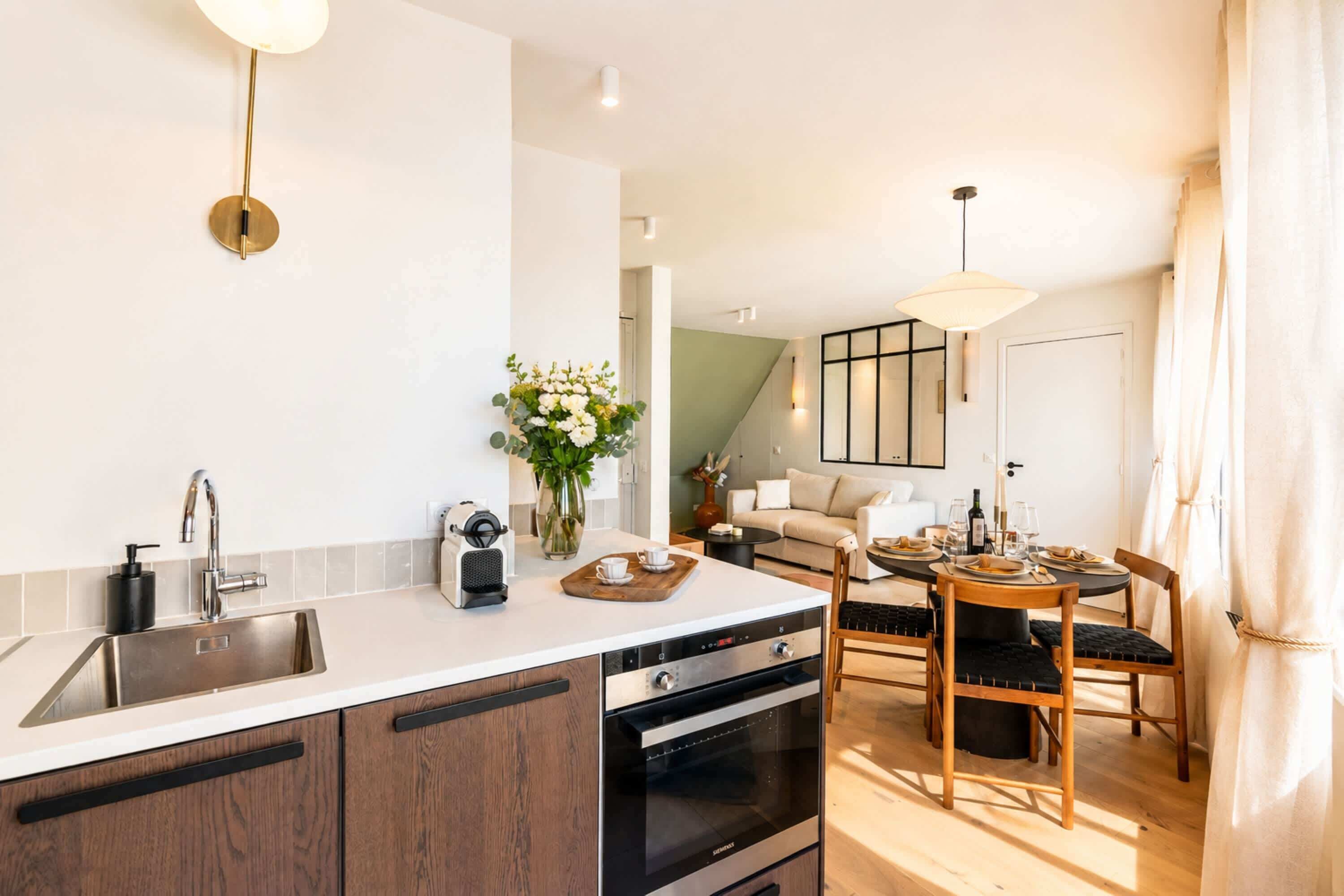 Una cocina moderna con horno integrado, cafetera y comedor con mesa lista para dos.