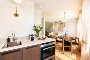 A modern kitchen with a built-in oven, a coffee machine, and a dining area with a table set for two. - Loft with terrace, jacuzzi & lift near Invalides (Paris)
