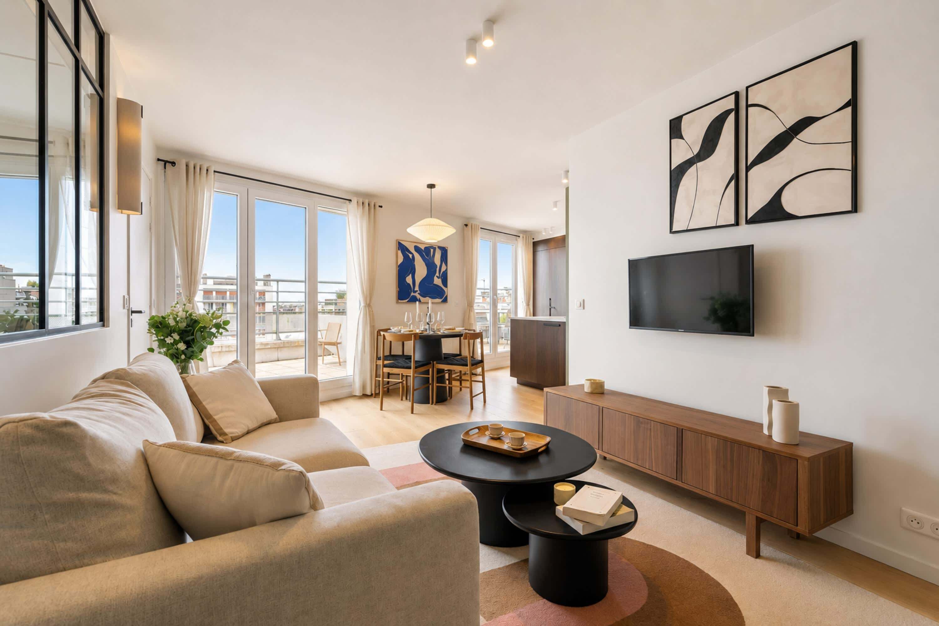 A modern living room with a sofa, a coffee table, a dining area with chairs, and a TV mounted on the wall.