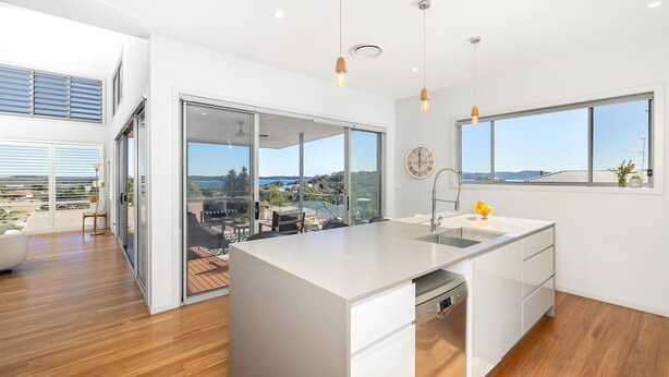 A modern kitchen with a large island, a view of the outdoors, and a dining area with a view. - The Family Tide – large family home, entertaining deck with views, swimming pool, air conditioning (Corlette)
