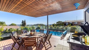 A wooden deck with a pool, outdoor furniture, and a grill area. - The Family Tide – large family home, entertaining deck with views, swimming pool, air conditioning (Corlette)